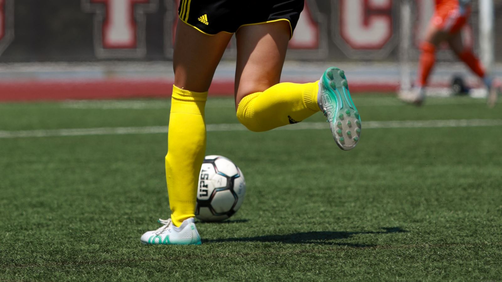 Photo of a women's soccer player waist down, sprinting on field dribbling ball, wearing IDA Rise women's white soccer cleats.