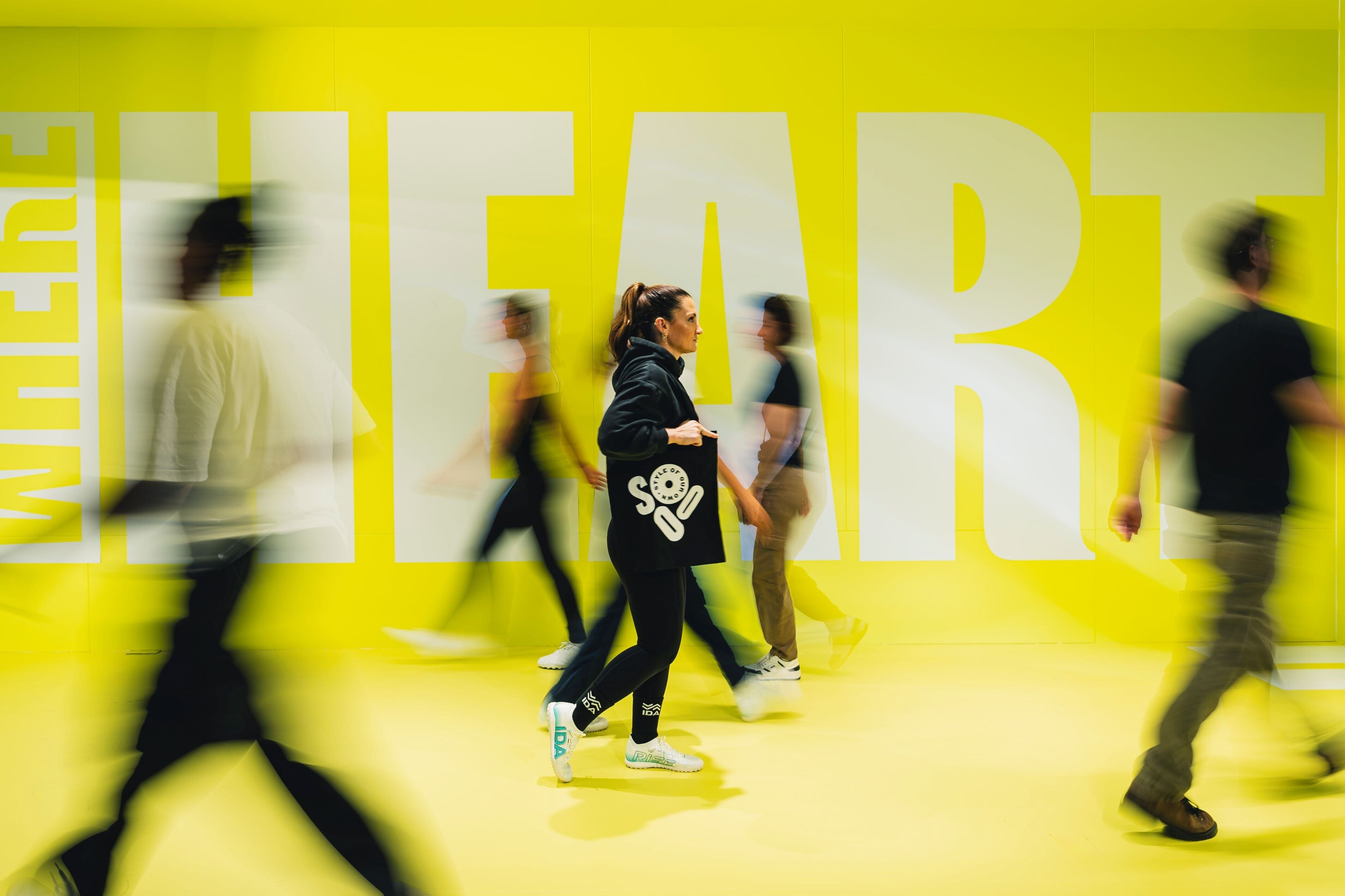 Graphic Image of people walking and blurred out except for one woman walking, wearing IDA shoes and holding a SOOO tote bag.