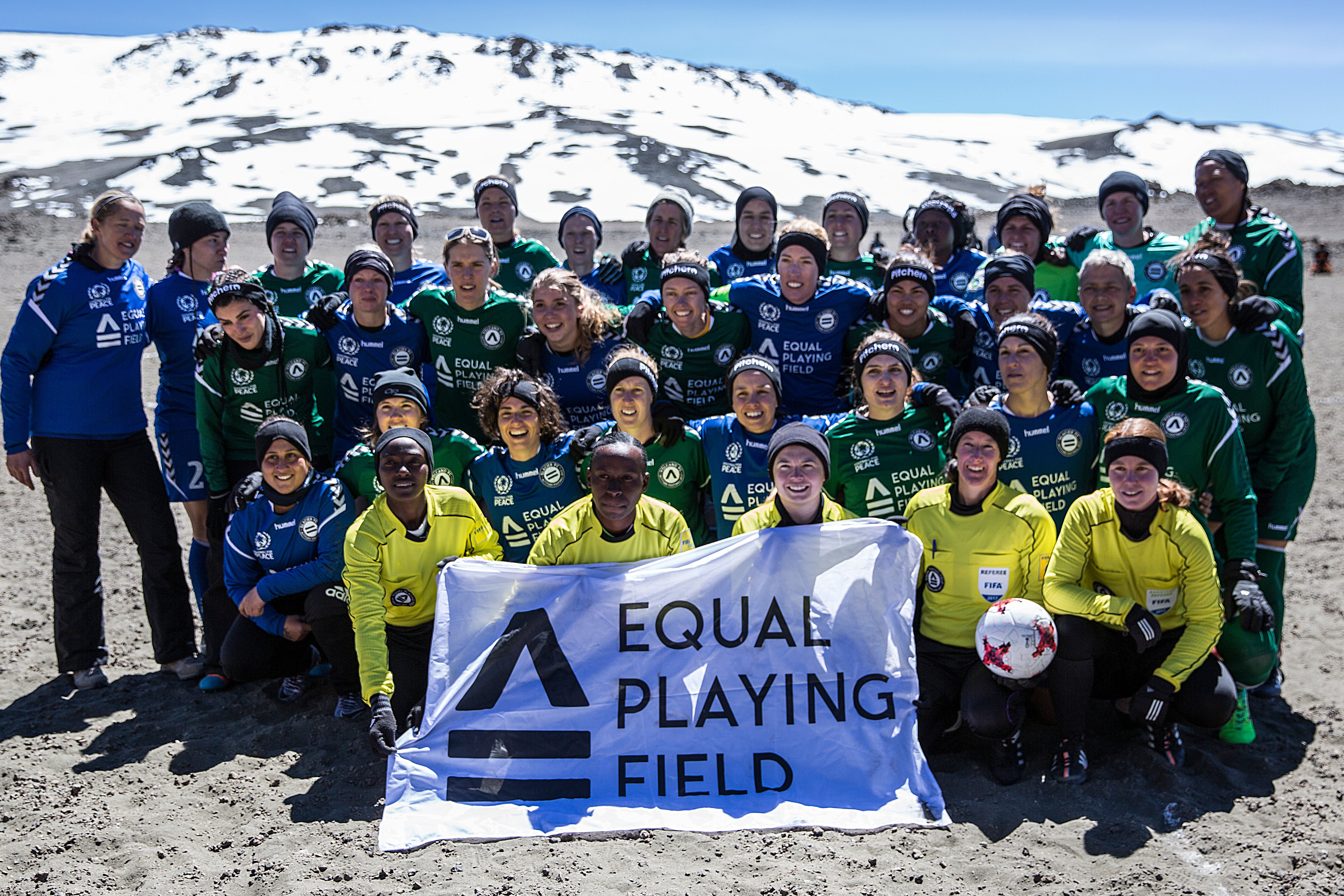 Group of soccer players in green and blue jerseys pose with referees and an Equal Playing Field banner after setting world record on top of Mount Kilimanjaro