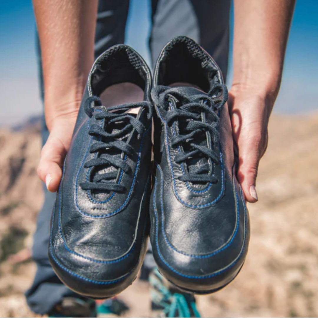 Two hands holding the prototype pair of IDA women's soccer cleats.