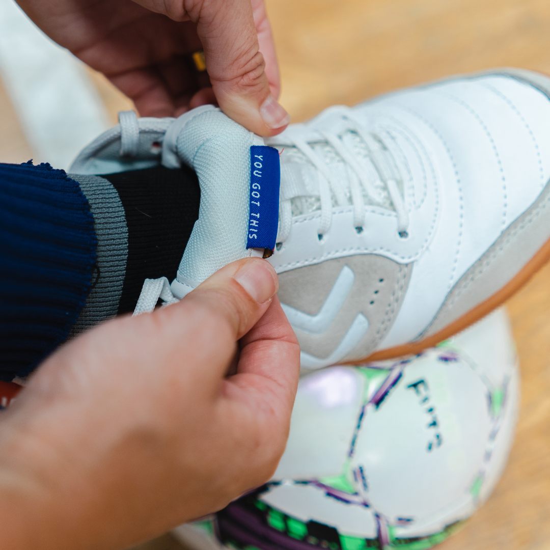 Close up shot of a player wearing the IDA Spirit white indoor soccer shoes while folding back the tongue of the shoe to reveal the text "You Got This".