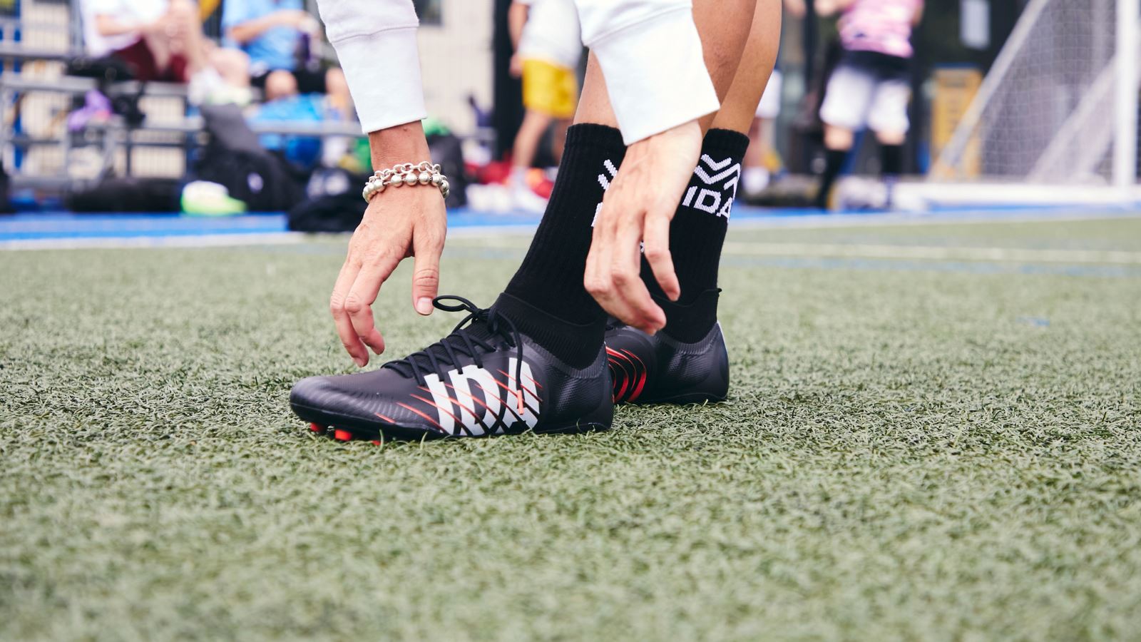 Close up photo of a woman tying her black soccer cleats on a turf field. 