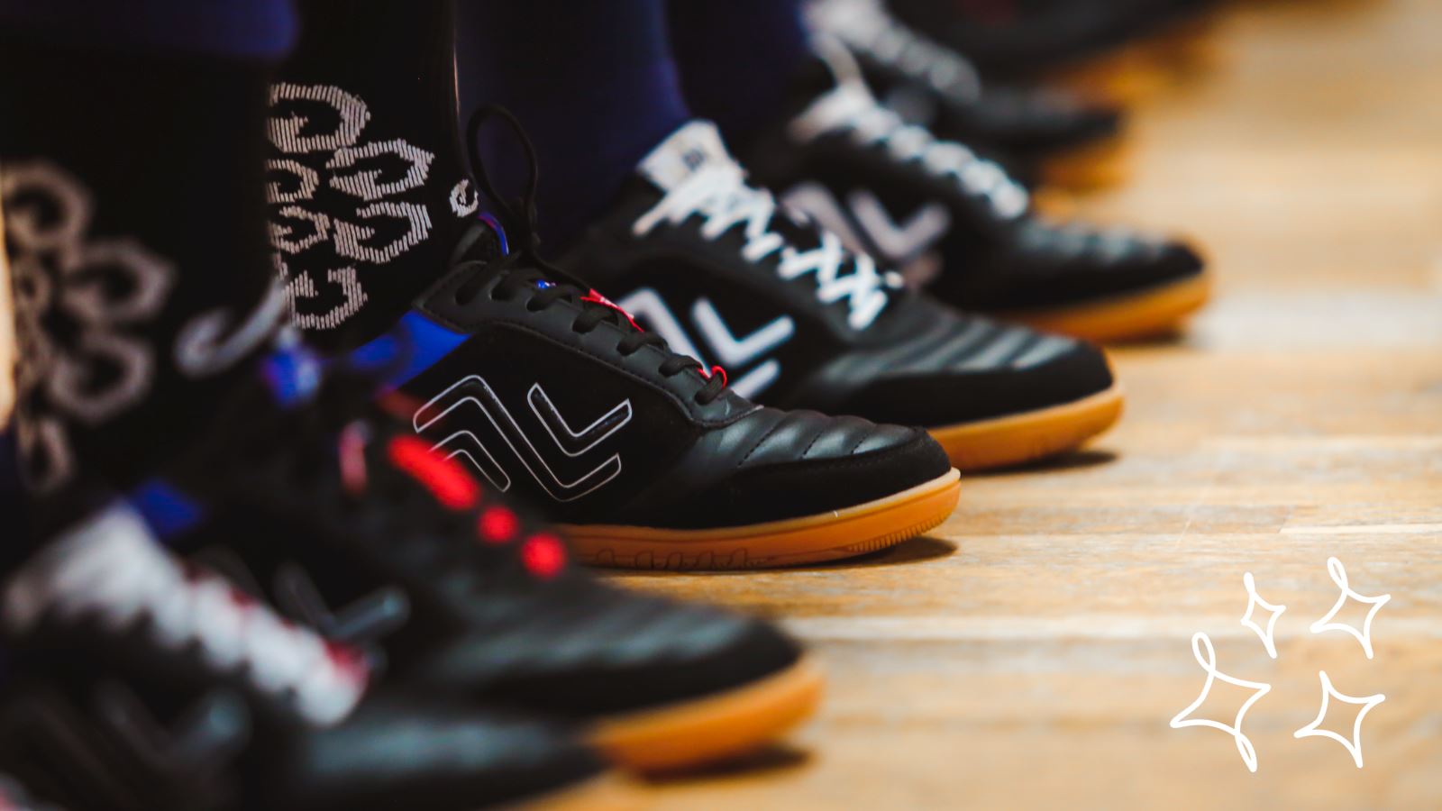 Close up of black IDA Spirit indoor women's soccer shoes in a line on a futsal court.