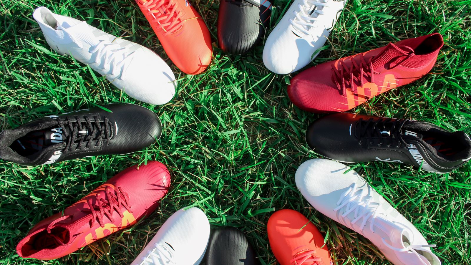 IDA women's specific soccer cleats in a circle on grass. Black IDA Rise, White IDA Rise, Red IDA Rise, White IDA Centra